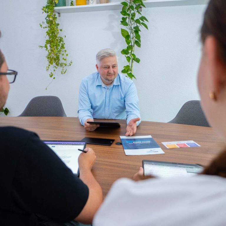 Geschäftsmeeting mit einer Person, die ein Tablet hält, und zwei anderen Personen am Tisch.